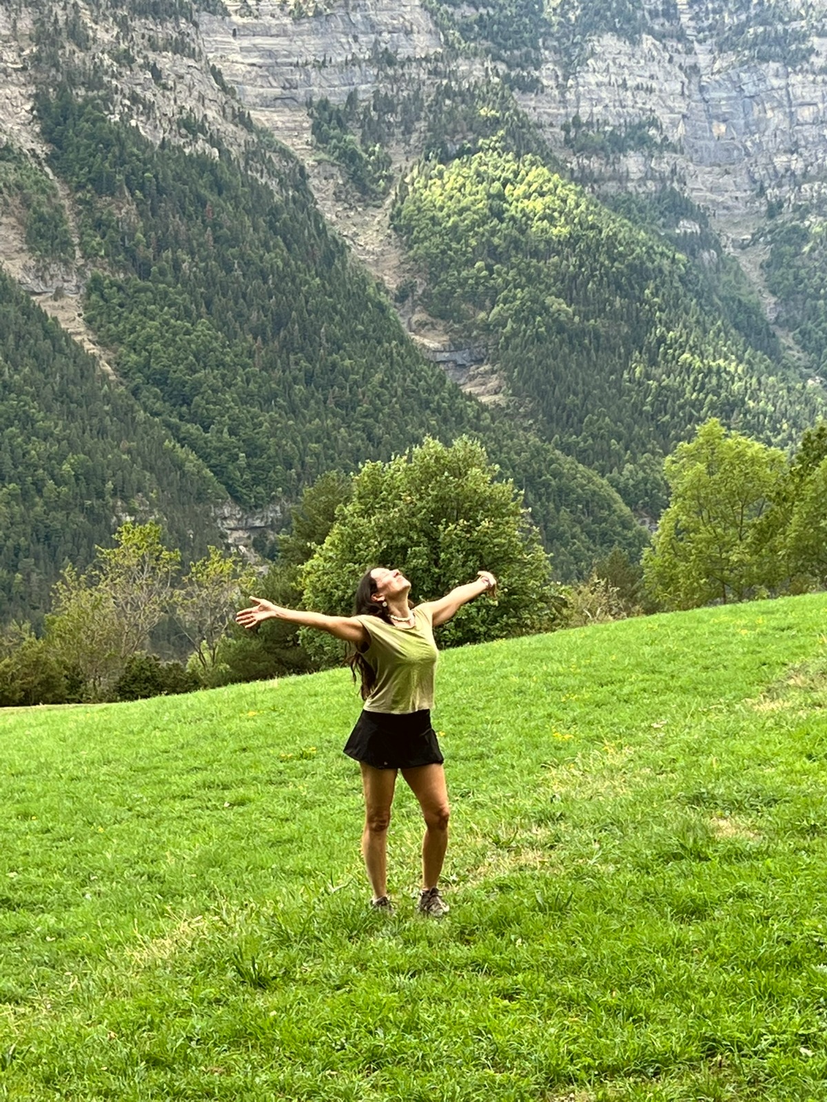 Mariví Perlor con los brazos abiertos hacia el cielo en una pradera de montaña