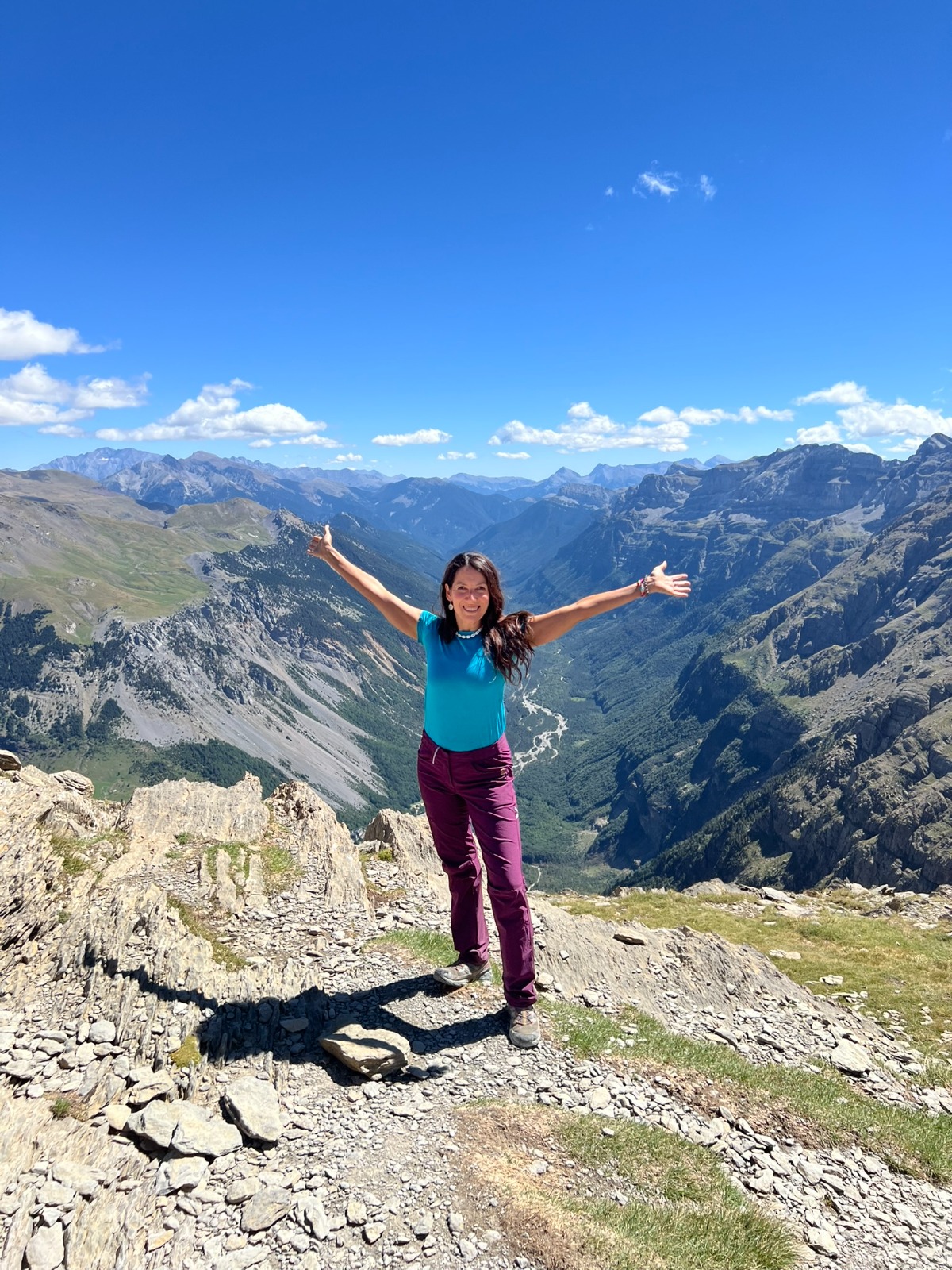 Mariví Perlor con los brazos abiertos en la cima de una montaña, ante el valle