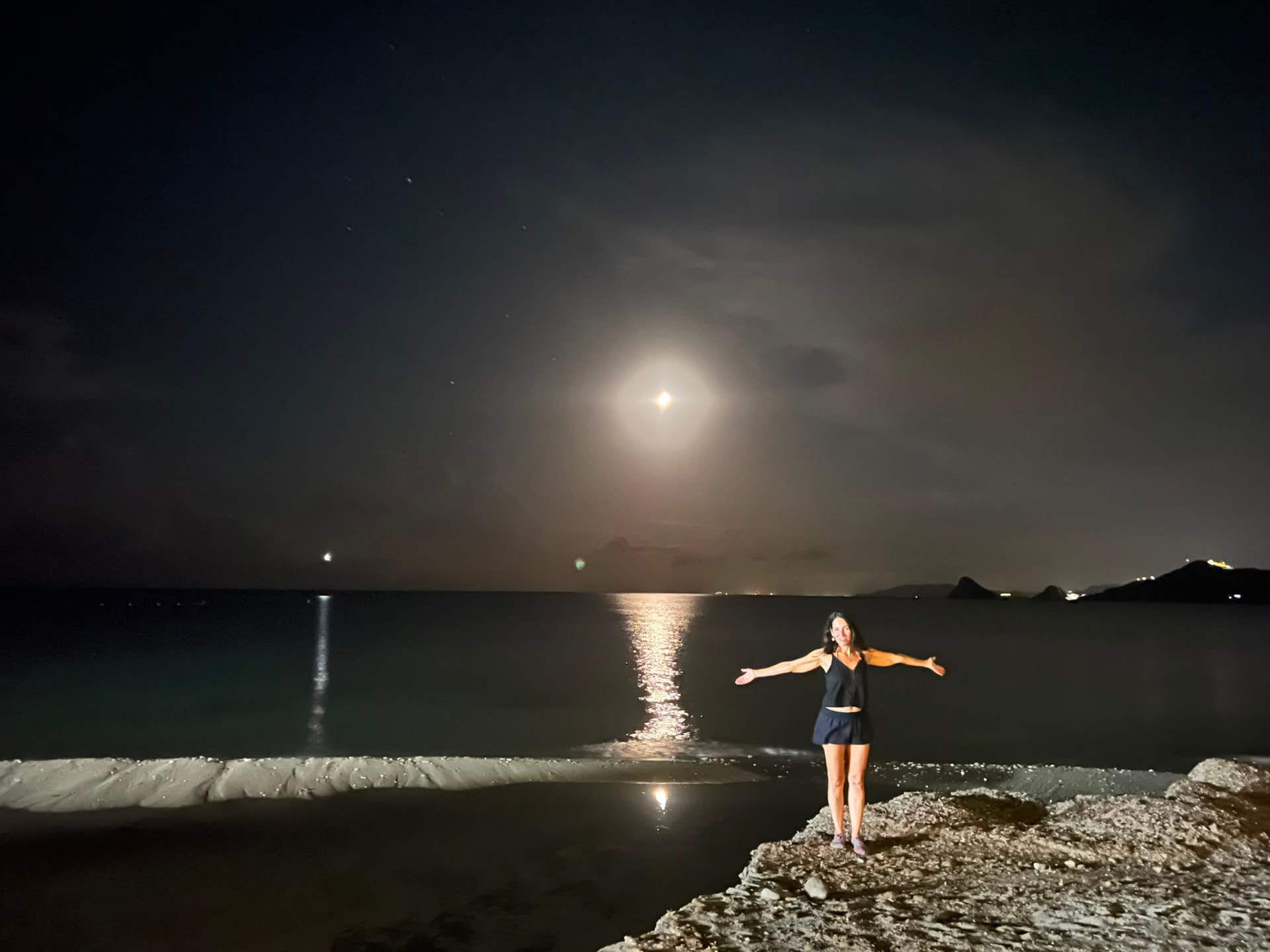 Mariví Perlor con los brazos abiertos bajo la luna llena, junto al mar de noche